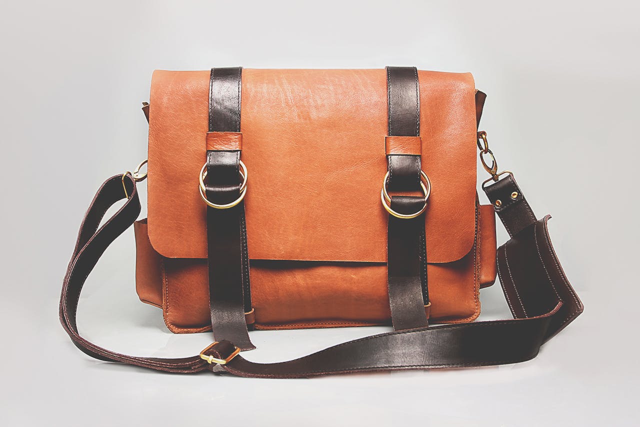 Elegant brown leather briefcase with dark straps and metal buckles, ideal for fashion and business.